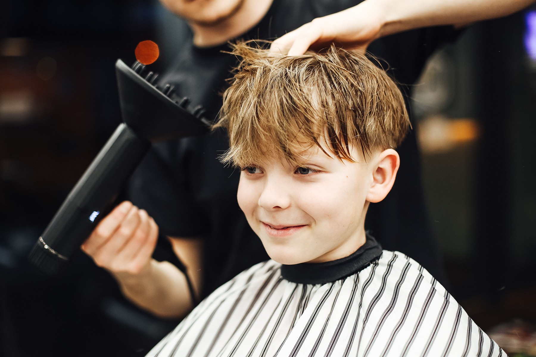 Barber suszy suszarką i stylizuje włosy chłopca w salonie fryzjerskim dla dzieci BRODSKI w Wilanowie.