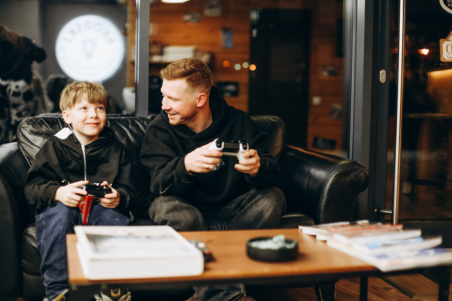Ojciec i syn grają na konsoli Xbox w strefie relaksu salonu barberskiego BRODSKI w Wilanowie.