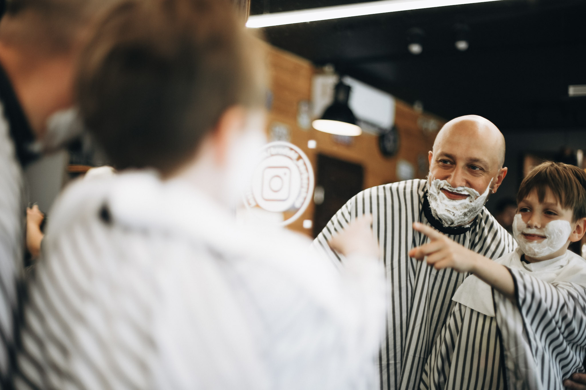 Ojciec i syn z pianą do golenia na twarzach śmieją się razem w lustrze barberskim — rodzinne strzyżenie w BRODSKI Barbershop Wilanów