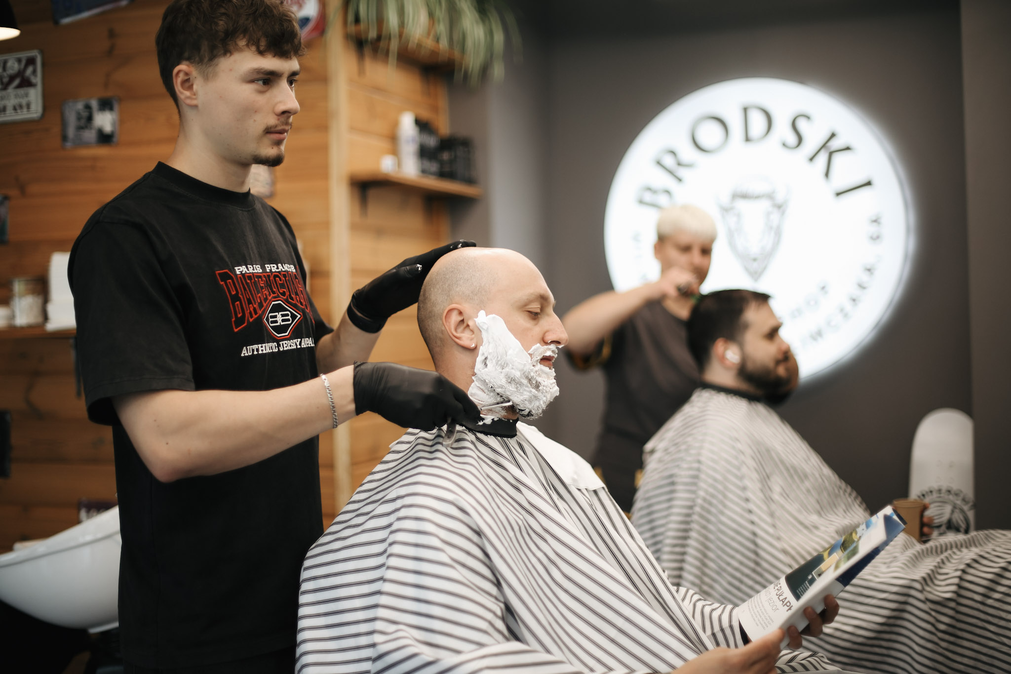Barber nakłada pianę do golenia na głowę klienta brzytwą w BRODSKI Barbershop Wilanów, Warszawa