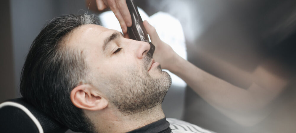Professional barber trimming client's beard with precision razor at BRODSKI barbershop Wilanów